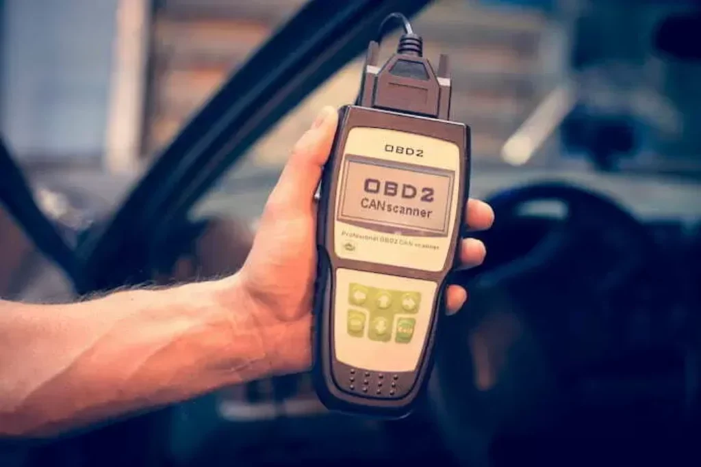 Mão com scanner automotivo e ao fundo um carro